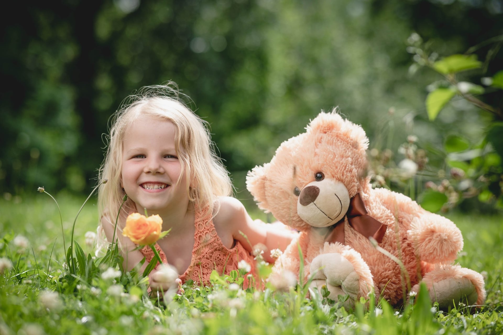 Kind liegt lachend mit Teddybär im Gras