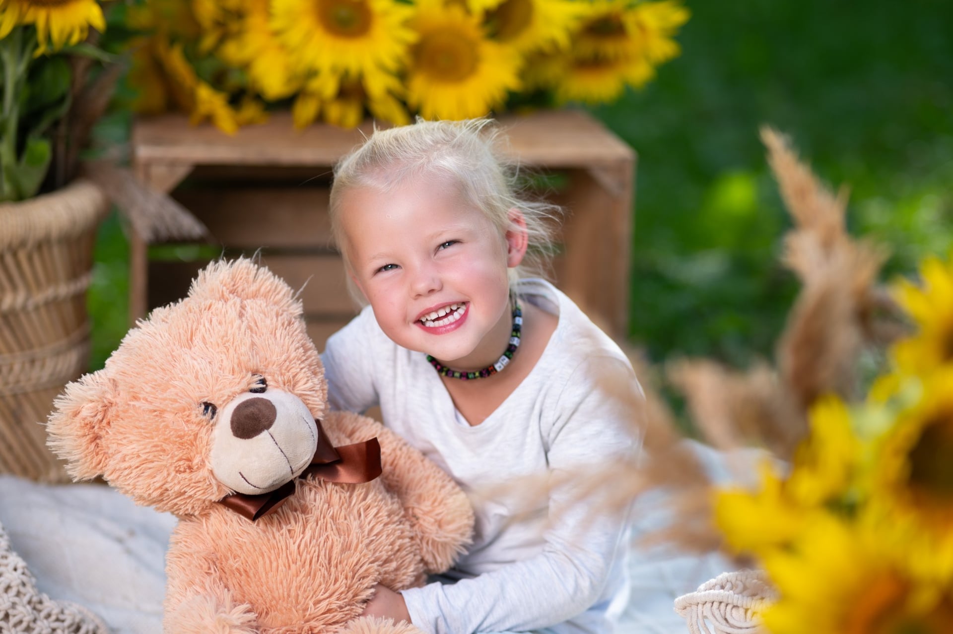 Kind lacht herzlich und hält einen Teddybären, im Hintergrund Sonnenblumen